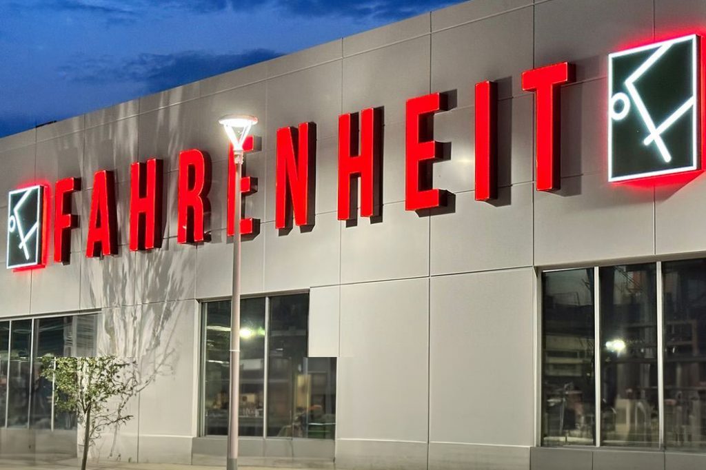 The Fahrenheit restaurant sign glows red at dusk, with the stylized logo on either side, against a contemporary building facade.