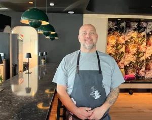 Chef Rocco Whalen smiling in a charcoal apron inside Fahrenheit Cleveland