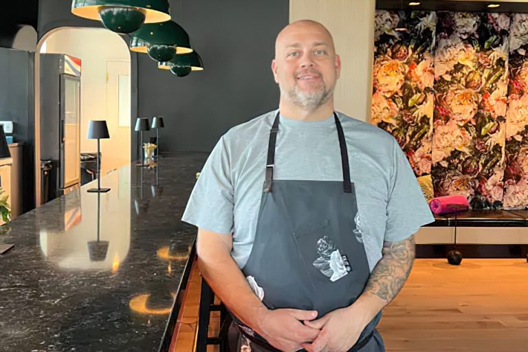 Chef Rocco Whalen stands smiling in a charcoal apron inside the newly designed Fahrenheit Cleveland, embodying contemporary American cuisine.